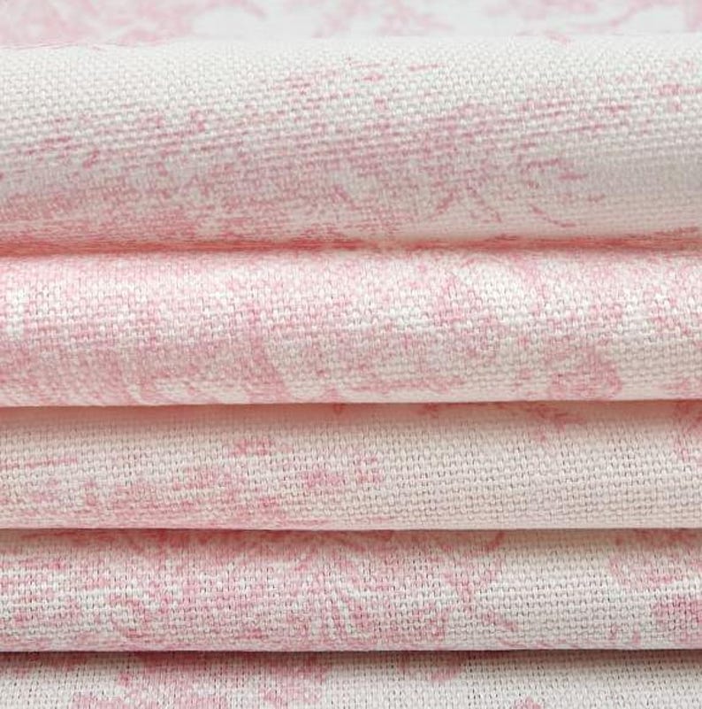 May include: Close-up of folded fabric with a pink floral pattern on a white background. The fabric is stacked in layers, showcasing the texture and design. The pink pattern is a soft, watercolor-like design.