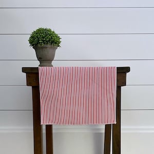 May include: Red and white striped table runner on a wooden table with a small potted plant.