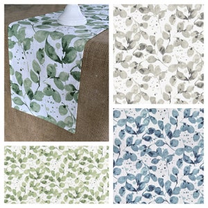 May include: A set of three table runners with a watercolor leaf pattern. The runners are in green, gray, and blue.
