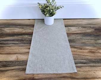 May include: A light gray linen table runner with a subtle texture. The runner is laid out on a wood floor.