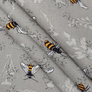 May include: Gray fabric with a repeating pattern of black and yellow bees. The bees are stylized and have a cartoonish appearance.