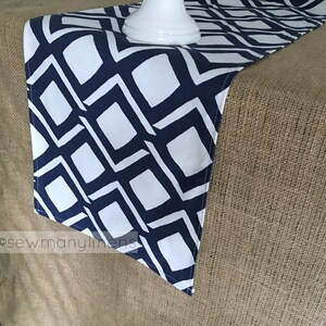May include: A white and navy blue geometric table runner with a diamond pattern. The runner is on a hessian surface.