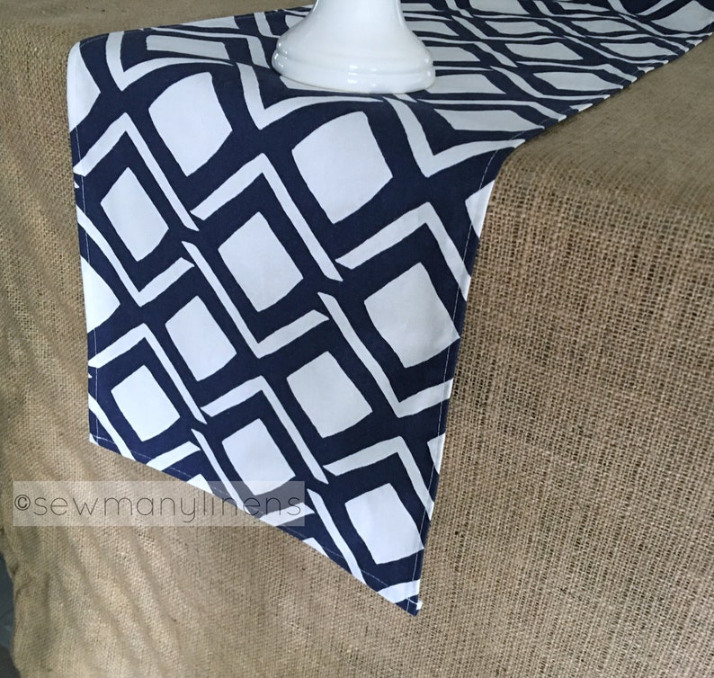 May include: A white and navy blue geometric table runner with a diamond pattern. The runner is on a hessian surface.