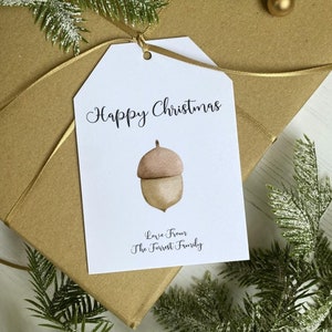 Op de afbeelding: Witte cadeaukaart met de tekst "Happy Christmas" en een aquarel-illustratie van een eikel. De tekst "Love from The Forrest Family" staat onder de eikel gedrukt.