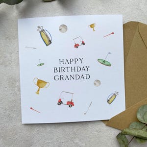 May include: A square white birthday card with the words "HAPPY BIRTHDAY GRANDAD" and golf-themed illustrations. The card features golf balls, golf carts, golf bags, tees, and trophies. A brown envelope is included.