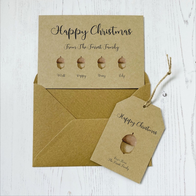 Op de afbeelding: Een bruine kaart met de tekst "Prettige Kerst" en "Van de familie Forrest". Er zijn vier eikels met de namen "Matt", "Poppy", "Daisy" en "Lily" eronder geschreven. Een bruine envelop en een bruin cadeau-etiket met de tekst "Prettige Kerst" en "Lieve groeten van de familie Forrest" zijn ook te zien.