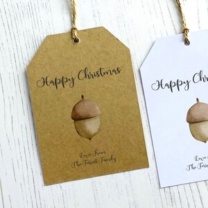 Op de afbeelding: Twee cadeaulabels met een bruine eikel-illustratie en de tekst "Prettige Kerst". Het label aan de linkerkant is bruin met de tekst "Liefde van de familie Forrest". Het label aan de rechterkant is wit.