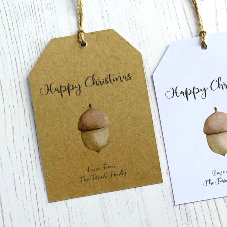 Op de afbeelding: Twee cadeaulabels met een bruine eikel-illustratie en de tekst "Prettige Kerst". Het label aan de linkerkant is bruin met de tekst "Liefde van de familie Forrest". Het label aan de rechterkant is wit.