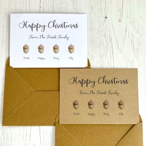Op de afbeelding: Twee kerstkaarten met een bruine kraftpapier achtergrond en witte tekst. De tekst luidt "Prettige Kerst" en "Van de familie Forrest". Elke kaart heeft vier eikels met namen eronder: Matt, Poppy, Duty, Lily.