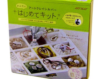 Könnte beinhalten: Eine grün-gelbe Schachtel mit der Aufschrift "ART CLAY" enthält ein Schmuck-Bastelset. Die Schachtel zeigt fertige Schmuckstücke. Das Set enthält Materialien und Anleitungen zur Herstellung einzigartiger Accessoires.