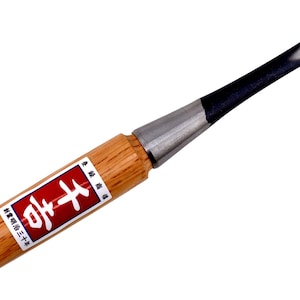 May include: A wood chisel with a wooden handle and a metal blade. The handle is light brown with a red and white label. The blade is black and silver. This woodworking tool is designed for shaping and carving wood.