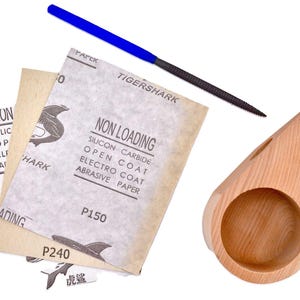 May include: Three sheets of sandpaper with a shark logo and the text "Non Loading Silicon Carbide Open Coat Electro Coat Abrasive Paper P150 P240" and a blue file with the text "Tiger Shark" and a wooden cup.