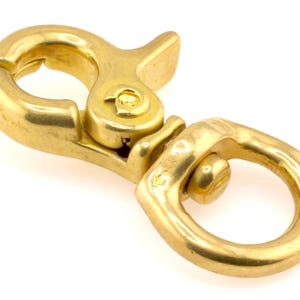 May include: A close-up of a gold-colored swivel snap hook. The hook has a spring-loaded clasp and a circular eyelet. The metal has a shiny finish and is set against a white background.