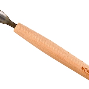 Puede incluir: Una gubia para tallar madera con una hoja curva de color plateado y un mango de madera marrón claro. El mango tiene texto japonés y medidas impresas. La herramienta está diseñada para proyectos detallados de carpintería y tallado.