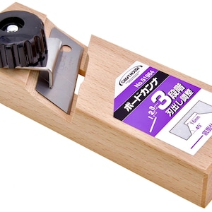 May include: A wooden hand plane with a black knob, a silver blade, and a purple and white label. The label has Japanese text and diagrams. The plane is designed for woodworking.