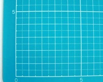 May include: A turquoise self-healing cutting mat with a grid pattern and white numbers 0 and 5 on the bottom and left sides.