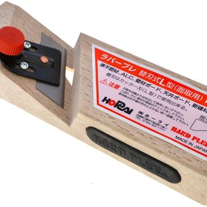 May include: A wooden hand plane with a black blade holder and a red adjustment knob. The plane has a rectangular shape with a blade set at an angle. A label with Japanese text is affixed to the side.