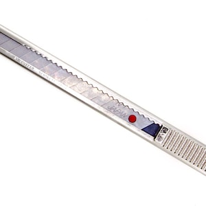 May include: A silver utility knife with a retractable blade. The knife has a ridged handle and a blade marked with the word "JAPAN" and a red dot. The blade is partially extended and has a serrated edge.