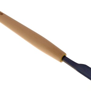 May include: A wood carving chisel featuring a long, cylindrical light-colored wooden handle and a dark blue metal blade. The handle displays small, dark, stamped Japanese characters near the end, and the metal blade has a curved, scoop-like shape.