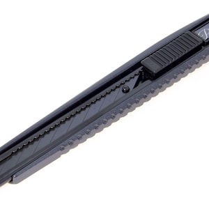 May include: A black utility knife with a retractable blade. The knife has a textured grip and a sliding mechanism for blade adjustment. The text "Premium" is printed on the top of the knife.