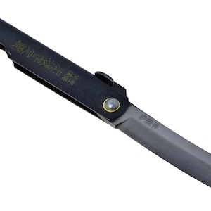 Könnte beinhalten: Ein schwarzes Klappmesser mit einer geraden Klinge und einem Griff, der mit goldenen japanischen Schriftzeichen verziert ist. Das Messer hat einen metallischen Drehpunkt mit einem gelben Ring und einen strukturierten Griff für eine dunkle Optik.