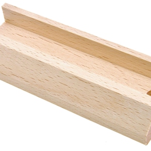 May include: A rectangular wooden block with a groove running along its length. The block is made of light-colored wood and has a small, circular hole on one end. The design is simple and functional.