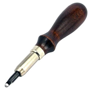 Puede incluir: Una herramienta de punzonado de cuero con mango de madera marrón, cabeza de metal y borde de corte circular.