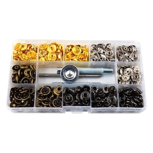 May include: A clear plastic organizer filled with various metal snap fasteners in gold, silver, and black. A silver metal tool is included for setting the snaps. The snaps are in different shapes and sizes.