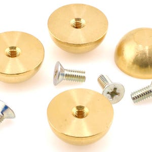 May include: A collection of brass furniture knobs and screws. The knobs are hemispherical with a flat top and a threaded hole. The screws are silver with a slotted or Phillips head. The hardware is on a white background.
