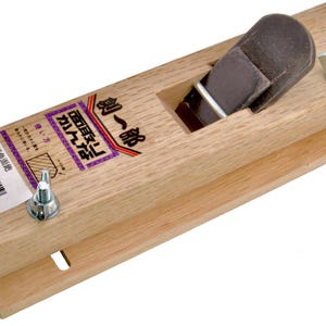 May include: A wooden block plane with a brown blade and a wooden body. The plane has a rectangular shape with a label on the side. The label has Japanese text and a barcode. The plane is designed for woodworking.