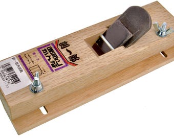 May include: A wooden block plane with a brown blade and a wooden body. The plane has a rectangular shape with a label on the side. The label has Japanese text and a barcode. The plane is designed for woodworking.