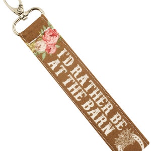 May include: A brown key chain with a floral design and the text "I'd rather be at the barn".