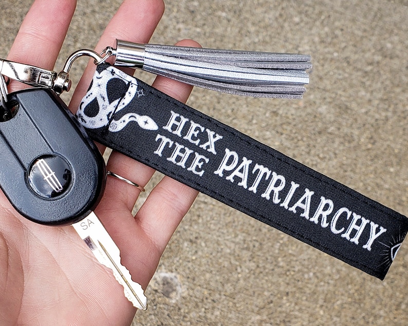 May include: Black key chain with a white snake design and the text "Hex the Patriarchy". The key chain has a silver tassel.