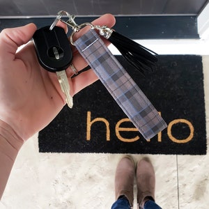 Peut inclure: Un porte-cl&eacute;s en tissu &agrave; carreaux gris et bleus avec un pompon noir. Le porte-cl&eacute;s est attach&eacute; &agrave; un anneau de cl&eacute; argent&eacute; et &agrave; une cl&eacute; de voiture noire.