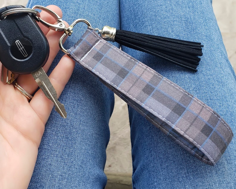 May include: A gray and blue plaid fabric keychain with a black tassel. The keychain is attached to a silver key ring and a car key.