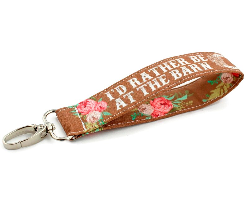 May include: Brown fabric key chain with white text that reads "I'd rather be at the barn" and floral print. The key chain has a silver metal clasp.