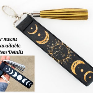 Puede incluir: Llavero negro con un dise&ntilde;o de sol y luna dorado. El llavero tiene un borla dorada y un anillo de llave plateado.  "Silver moons also available, see Item Details" est&aacute; escrito en la imagen.