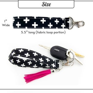 Peut inclure: Porte-cl&eacute;s en tissu noir et blanc avec un pompon rose. Le porte-cl&eacute;s mesure 5,5 pouces de long et 1 pouce de large. Le tissu pr&eacute;sente un motif r&eacute;p&eacute;titif de croix blanches sur fond noir.