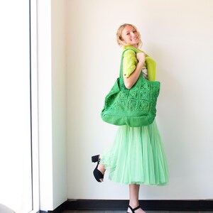 Puede incluir: Una mujer lleva un bolso tote de crochet verde, una falda verde y tacones negros. El bolso tiene un patr&oacute;n cuadrado.