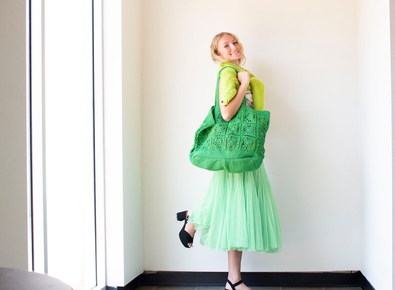 Puede incluir: Una mujer lleva un bolso tote de crochet verde, una falda verde y tacones negros. El bolso tiene un patr&oacute;n cuadrado.