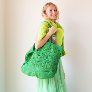 Puede incluir: Una bolsa de mano de crochet verde con un patr&oacute;n cuadrado. La bolsa la lleva una persona que lleva un c&aacute;rdigan verde y una falda verde.