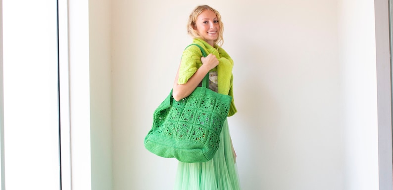 Puede incluir: Una bolsa de mano de crochet verde con un patr&oacute;n cuadrado. La bolsa la lleva una persona que lleva un c&aacute;rdigan verde y una falda verde.