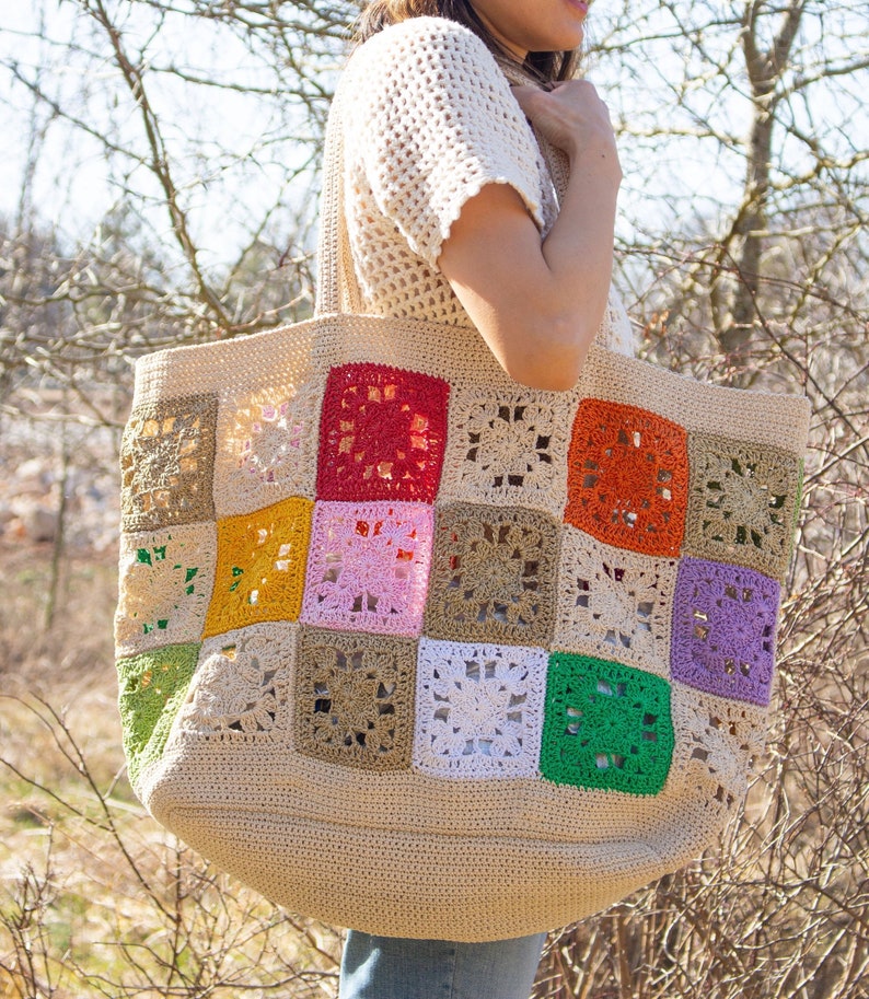 Puede incluir: Una gran bolsa de mano de crochet con un dise&ntilde;o de patchwork. La bolsa est&aacute; hecha de hilo beige con cuadrados coloridos en tonos de verde, rojo, naranja, amarillo, rosa, morado y blanco.