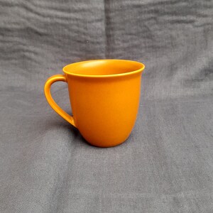 May include: A solid orange ceramic mug with a rounded handle.