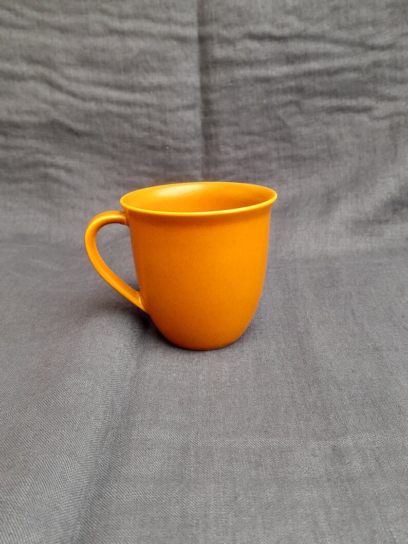 May include: A solid orange ceramic mug with a rounded handle.