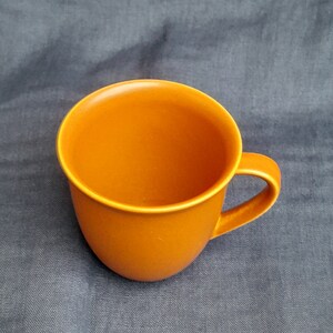 May include: A solid orange ceramic mug with a rounded shape and a handle.
