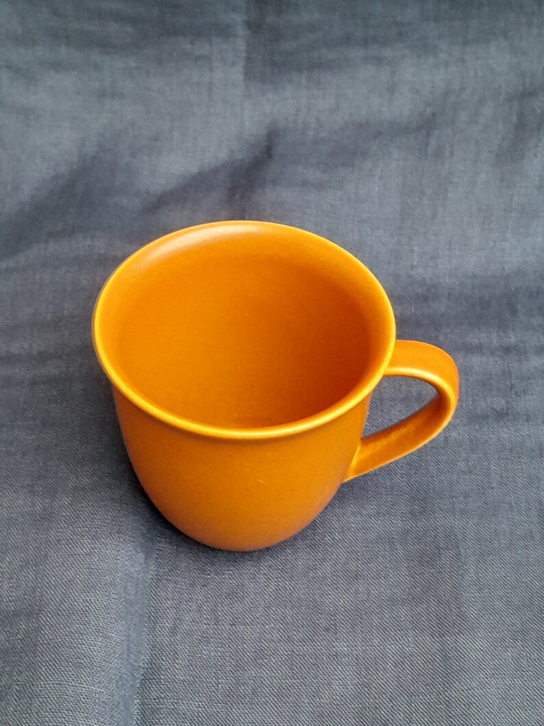 May include: A solid orange ceramic mug with a rounded shape and a handle.
