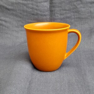 May include: A solid orange ceramic mug with a rounded shape and a handle.