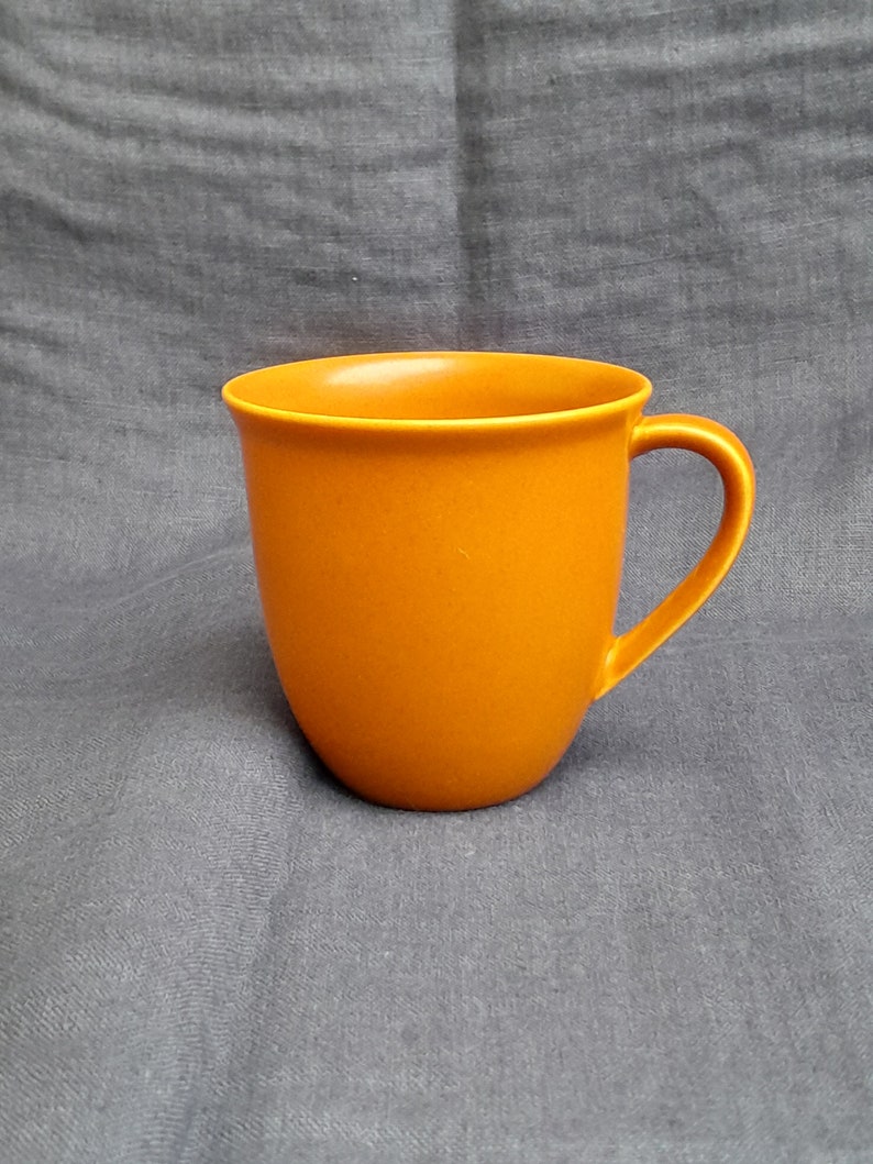 May include: A solid orange ceramic mug with a rounded shape and a handle.