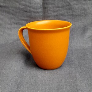 May include: A solid orange ceramic mug with a rounded handle.